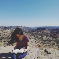 Photo of Kai reading a book with a mountain landscape behind her.